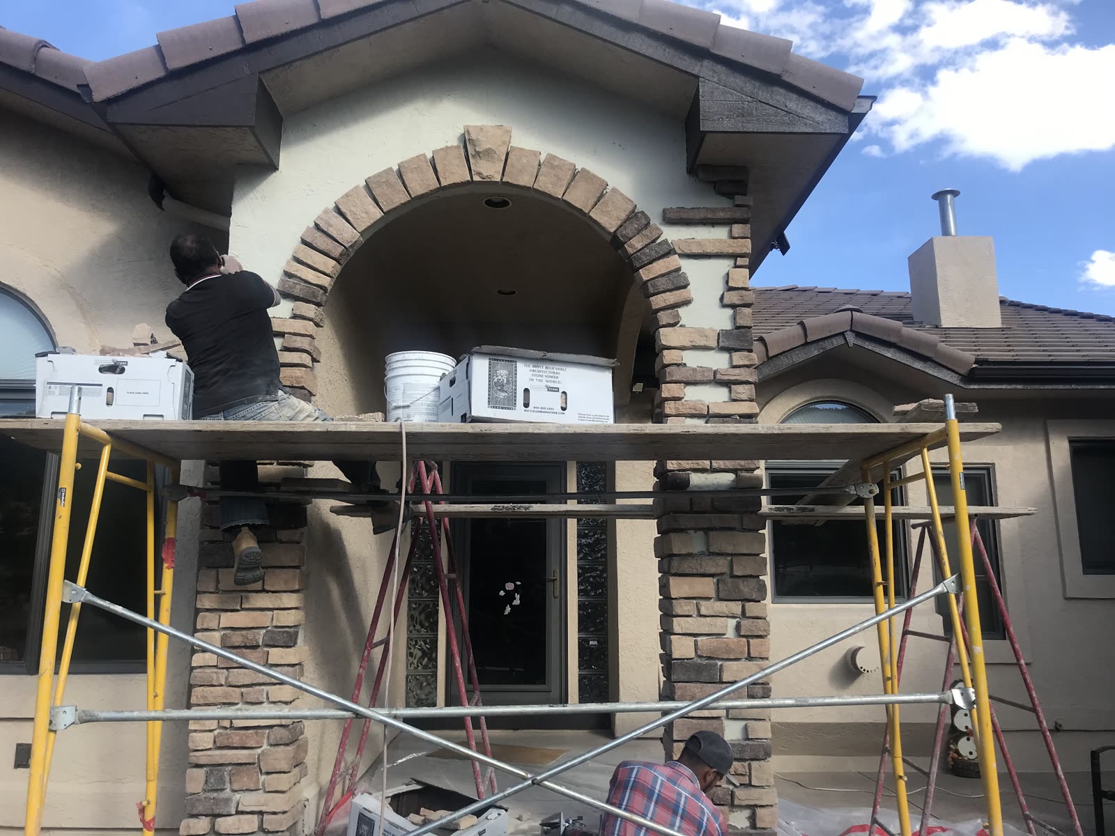 Fox Coatings crew on scaffolding repairing stucco and stone veneer around an arched entry on a Colorado Springs home